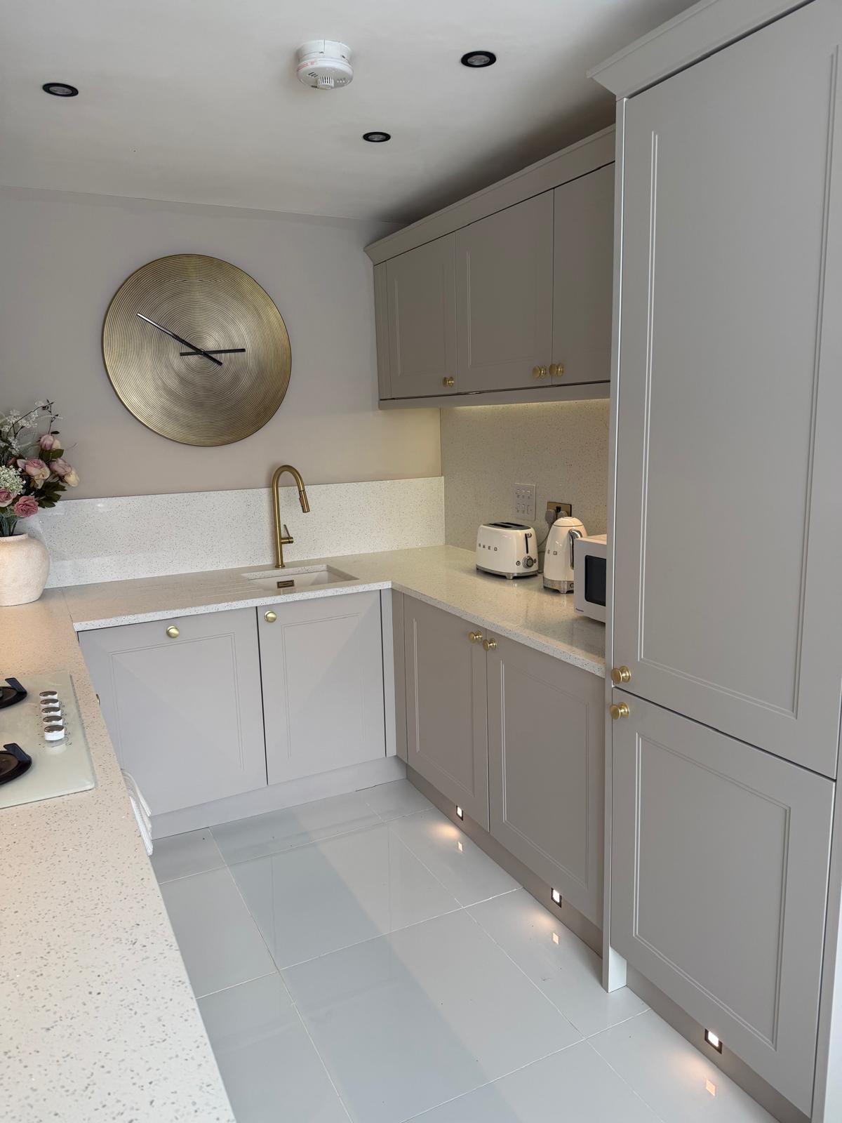 Kitchen sink area after renovation, with light grey shaker units, brass tap and pantry storage